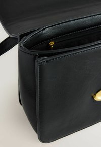 Must mustra, millel on lukuklapp ja kuldne pandla, osaliselt avatud, et näidata sisekatte ja õmbluste detaile.
