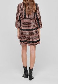 Short-sleeved dress with multicolored geometric patterns in black and pink, featuring a tiered design and relaxed fit, paired with black ankle boots.