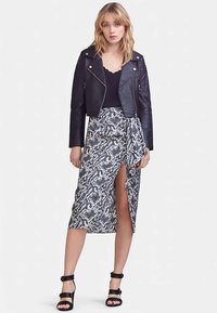 Czarna skórzana kurtka motocyklowa na czarnym topie, zestawiona z ołówkową spódnicą z czarno-białym wzorem w skórę węża, z rozcięciem z boku. Czarne sandały na obcasie z paskami.