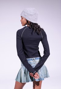 Cămașă neagră cu mâneci lungi și cusături contrastante, asociată cu o fustă mini plisată din denim decolorat. O căciulă gri cu model în rib completează ținuta.