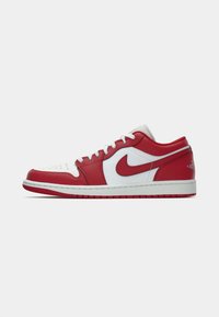 Sapatilhas Nike de cano baixo em vermelho e branco, com atacadores brancos, logotipo swoosh vermelho e biqueira perfurada, sobre um fundo branco.