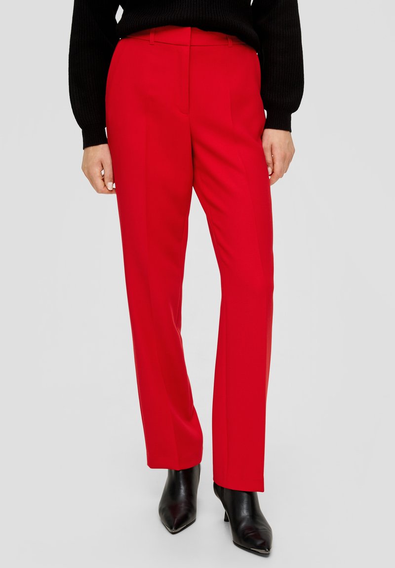 Czerwone dopasowane spodnie z gładkiego materiału, prosty krój nogawki i boczne kieszenie, w połączeniu z czarnymi botkami na obcasie w kształcie szpicy.