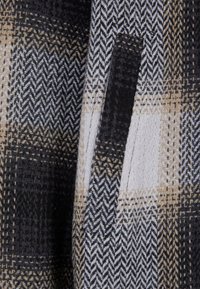 Tkanina w wzór jodełki i kratkę w kolorze czarnym, beżowym i białym, z pionowym otwarciem kieszeni i widocznym przeszyciem.