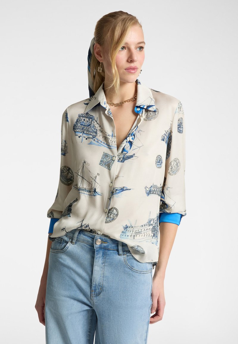 Blusa di seta con stampa nautica blu su sfondo beige, con un dettaglio blu sulle maniche e una vestibilità rilassata.