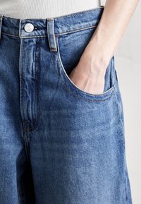 Pantalones cortos de mezclilla en azul claro con un corte holgado, que cuentan con un cierre de botón clásico, bolsillos laterales y detalles de costura visibles.