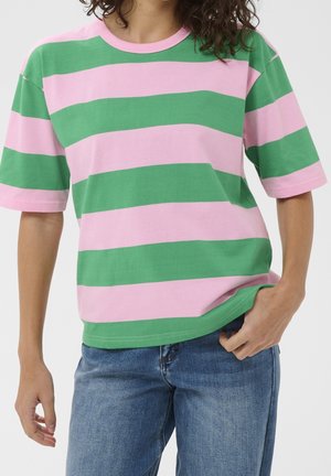Person wearing a pink and green wide horizontally striped short-sleeve t-shirt with blue jeans, standing against a plain background.