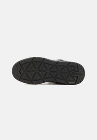 Suola di scarpa in gomma nera con un motivo geometrico testurizzato, caratterizzata da una punta arrotondata e dettagli del logo. Progettata per trazione e stabilità.