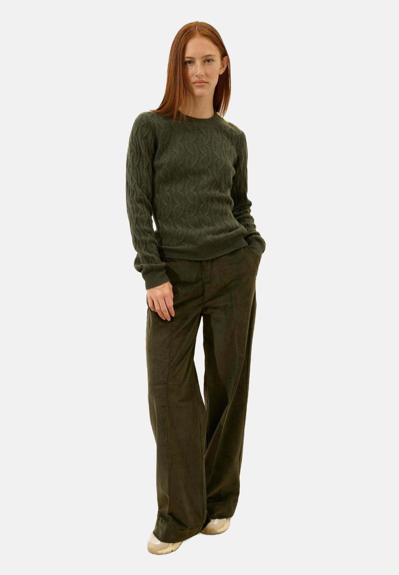 Oliwkowy sweter dzianinowy o fakturowanym wzorze, w połączeniu z szerokimi oliwkowymi spodniami z kordurowej tkaniny i beżowym obuwiem.
