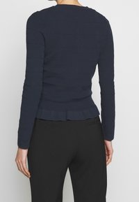 Námořnický top s dlouhými rukávy, texturovaným ribbovaným vzorem, skládáním na spodním okraji a kulatým výstřihem. V kombinaci s černými slim kalhotami.