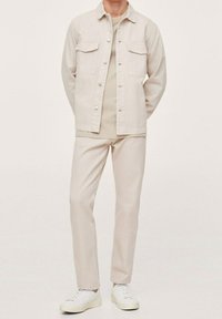 Chaqueta de mezclilla de color claro con dos bolsillos en el pecho, combinada con pantalones a juego y zapatillas blancas, con un diseño simple y corte recto.