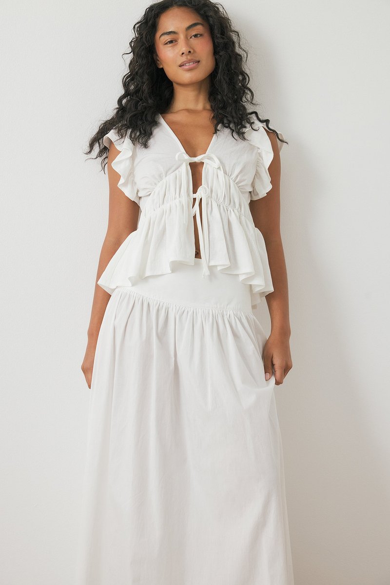 Witte twee-delige outfit met een ruffled top met korte mouwen en een strik aan de voorkant, en een lange, geraffineerde rok met een elastische tailleband.