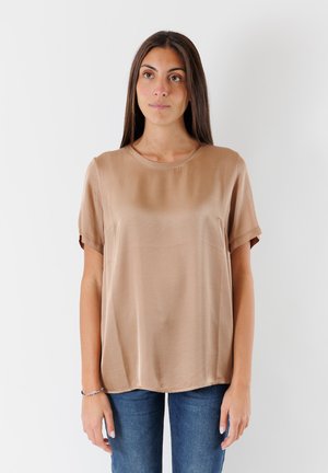 Top a maniche corte e collo rotondo in tessuto beige chiaro, con una texture liscia, dettagli delle cuciture sottili e una vestibilità rilassata. Abbinato a jeans blu.