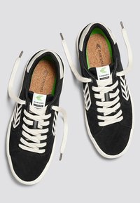 Schwarze Wildledersneaker mit weißen Schnürsenkeln und Akzenten. Verfügt über ein grünes Innenfutter, geprägtes Branding und strukturierte Sohlen. Lässiges Design.
