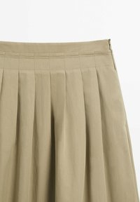 Jupe plissée couleur kaki avec ceinture cousue et fermeture éclair sur le côté, présentée sur fond blanc.