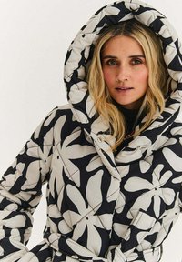 Prošívaný péřový kabát s kapucí v černé a béžové barvě, zdobený květinovým vzorem, s velkou kapucí a zavazováním v pase, který nabízí strukturovaný vzhled.