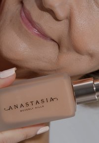 Beige vloeibare foundation in een frosted glazen fles met een zilveren pomp. Het etiket leest "ANASTASIA BEVERLY HILLS" in elegante zwarte letters.
