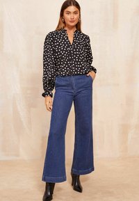 Blusa bianca e nera a pois con colletto, abbinata a jeans in denim blu a vita alta e gamba larga e stivaletti neri.