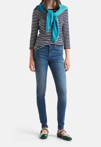 Randig långärmad skjorta i marinblått och vitt, turkos tröja knuten runt halsen, blå skinny jeans, gröna ballerinas med glansig yta.