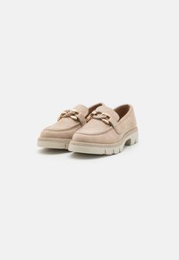 Beige semskede loafers med en kraftig hvit såle, med en dekorativ gullkjede over vamp. Rund tå og sømdetaljer.