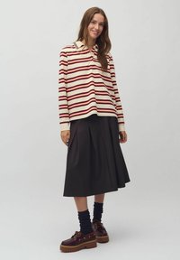 Gestreepte langetermijn poloshirt in crème, rood en donkerbruin, gecombineerd met een donkere plissé rok en bruine plateauschoenen met gouden accenten.