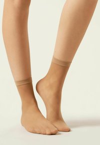 Beige ankelstrømper med en gennemsigtig tekstur, der har en solid kant øverst og et let diamantmønster i hele stoffet.