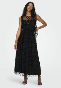 Abito maxi nero a pois realizzato in tessuto trasparente con dettagli a volanti, caratterizzato da una silhouette fluida e un design a strati.