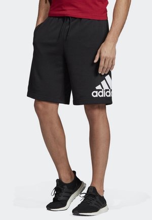 Czarne sportowe spodenki wykonane z miękkiego materiału z elastycznym pasem. Na lewej udzie znajduje się biały logo Adidas. Noszone z czarnymi trampkami.