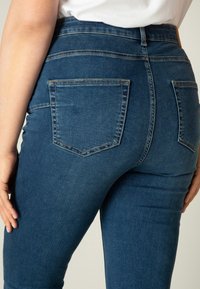 Hoge taille blauwe denim jeans met twee achterzakken, met een gladde textuur en subtiele vervaagde details langs de naden.