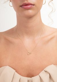 Goudkleurige halsketting met twee verstrengelde ronde schakels. De ketting heeft een fijne textuur en wordt gedragen op blote huid.