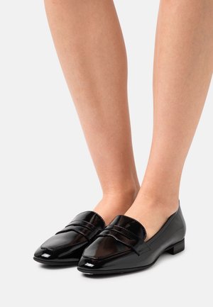 Sorte loafers i lakeret læder med lav hæl, der har en rundet tå og et dekorativt bånd over vristen. Glat, skinnende tekstur.