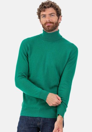Pull à col roulé vert en tissu doux, avec des manches longues et une coupe ajustée, associé à un jean denim bleu.