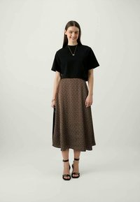Black cropped t-shirt, brown skirt with small white polka dots, ankle-strap black heels, simple silver necklace, model standing against plain background.