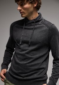 Suéter de color gris oscuro con cuello de capucha, cordones, puños acanalados y tejido texturizado. Presenta un diseño ajustado y detalles de costura sutiles.