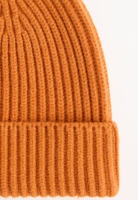 Orangene Strickmütze mit dicken vertikalen Rippen und umgeschlagenem Bündchen, vor einem weißen Hintergrund präsentiert.