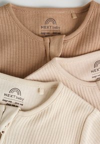 Drei gerippte Oberteile in Beige- und Cremetönen, mit Rundhalsausschnitten und kleinen Knopfverschlüssen. Die Etiketten zeigen die Marke "NEXT baby".