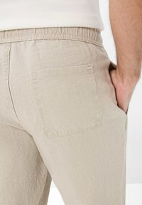 Beige linen trousers featuring an elastic waistband, a single back pocket, and subtle texture, designed for comfort and ease of wear.