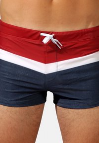 Shorts de bain rouge, blanc et marine avec un motif en chevrons, une taille à cordon et un tissu lisse et texturé.