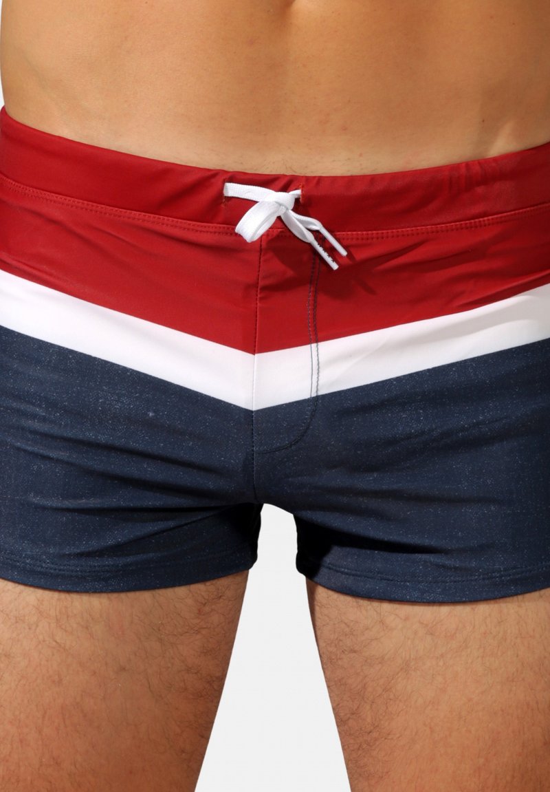 Shorts de bain rouge, blanc et marine avec un motif en chevrons, une taille à cordon et un tissu lisse et texturé.