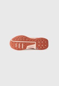 Semelle d'une sneaker avec une surface en caoutchouc texturé rouge, ornée d'un motif à mailles distinctif et d'accents de couleur claire.