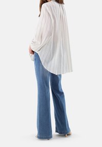 Blouse à rayures blanches avec manches larges, associée à un jean évasé bleu clair. La blouse présente une coupe décontractée et un ourlet arrondi.