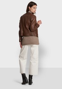 Bruine leren jas met een fitted ontwerp, gecombineerd met een beige trui en witte wijde broek. Zwarte enkellaarzen maken de outfit compleet.