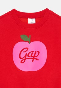 Sweatshirt roșu cu un grafic mare al unei mere roz, având o frunză verde și cu "Gap" scris cu litere cursive albe. Material moale și design cu guler rotund.