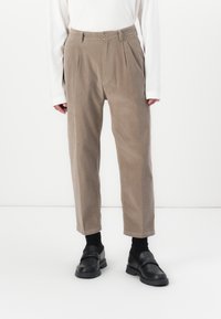 Lys brun kordfløyelsbukser med folder, tilpasset midje og rette ben, sammen med svarte loafers.
