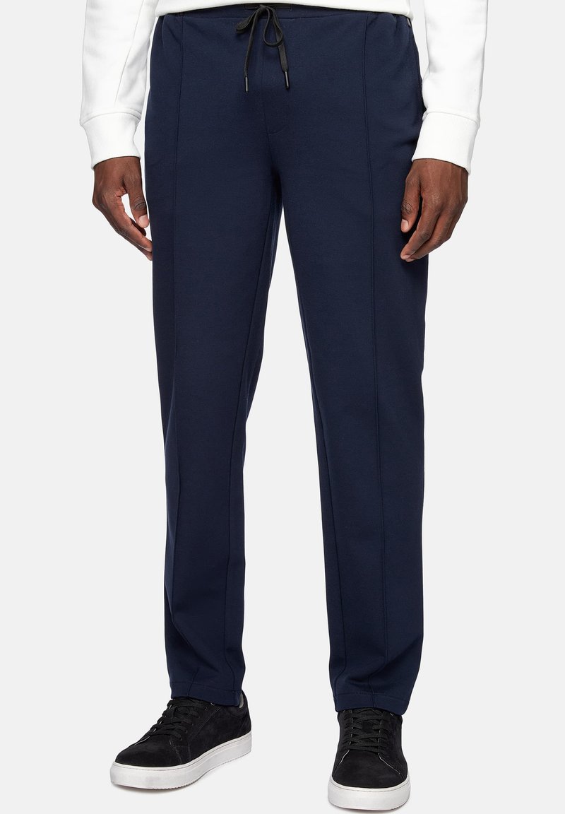 Navy blue sweatpants made of soft material, featuring a drawstring waist, side seam details, and a tapered leg. Black sneakers worn.