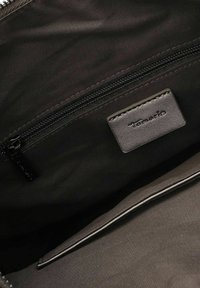 Intérieur d'un sac à main en tissu noir avec une poche zippée et une étiquette en cuir portant l'inscription "Tamaris". Texture lisse et design minimalist.