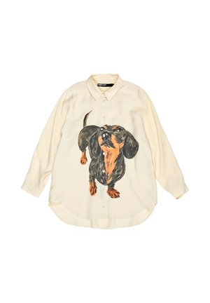Luźna kremowa koszula z namalowanym wzorem jamnika w czerni i brązie, zapinana na guziki, z długimi rękawami i zaokrąglonym dołem. Materiał o fakturze.
