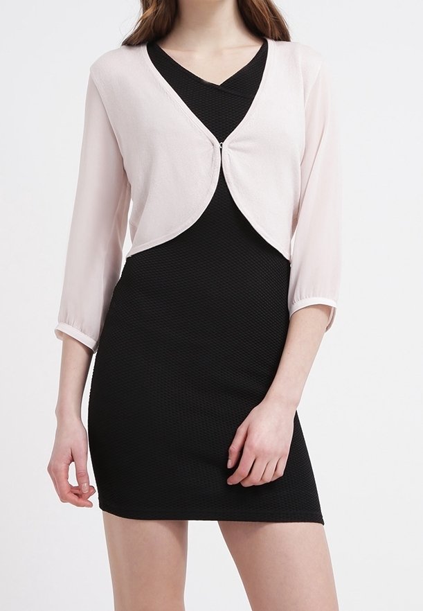 Femme portant une robe noire cintrée et texturée assortie à un boléro court rose clair à manches trois-quarts.