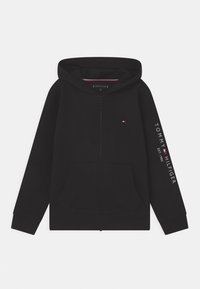 Schwarze Kapuzenjacke mit Reißverschluss, einer frontalen Tasche, gerippten Bündchen und einem kleinen Logo auf der Brust. Mit weißem Text entlang des linken ärmels. Weicher Stoff.