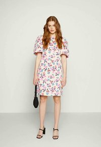 Vestido com padrão floral em rosa claro com mangas bufantes. Apresenta um corte reto, comprimento curto e é acompanhado por uma pequena bolsa preta.