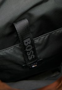 Wnętrze czarnej torby z materiału, z plecioną czarną etykietą z napisem "BOSS". Gładka tekstura z minimalnym przeszyciem i bez widocznych wzorów.